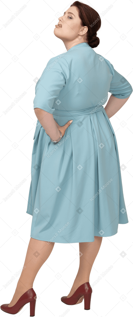 Side view of a woman in blue dress posing with hands on hips