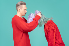 Handsome young man wearing purple wig on woman`s head