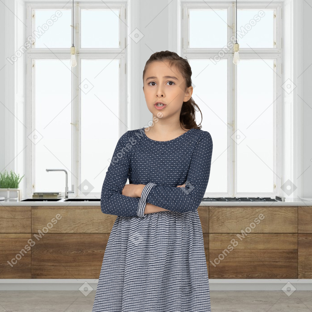 A little girl standing in a kitchen with her arms crossed