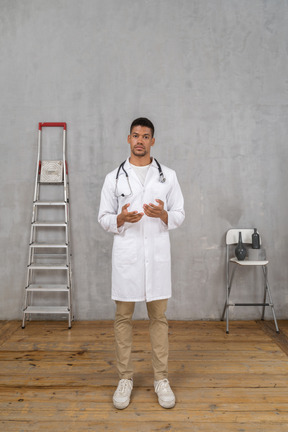 Vista frontal de un joven médico de pie en una habitación con escalera y silla explicando algo