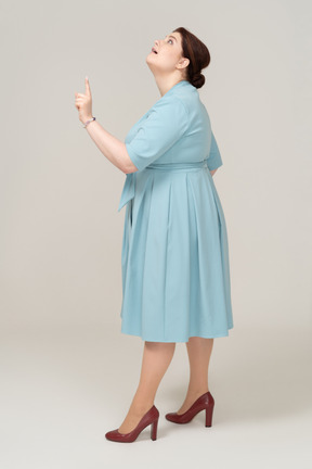 Vista lateral de uma mulher de vestido azul apontando para cima com um dedo