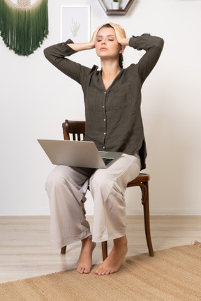 Three-quarter view of a busy young woman with a headache sitting on a chair with a laptop