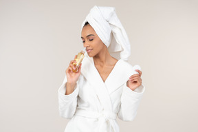 Black woman in white bathrobe and head towel enjoying her skin care routine