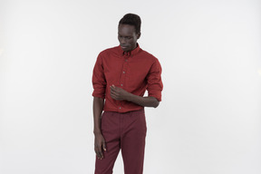 A young black man in a red shirt with rolled up sleeves and dark red pants standing alone on the white background