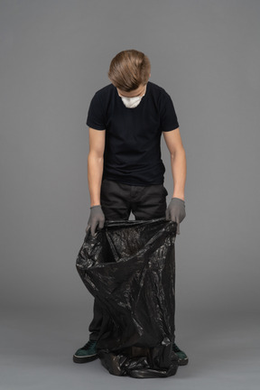 Un joven con una máscara y mirando dentro de una bolsa de basura