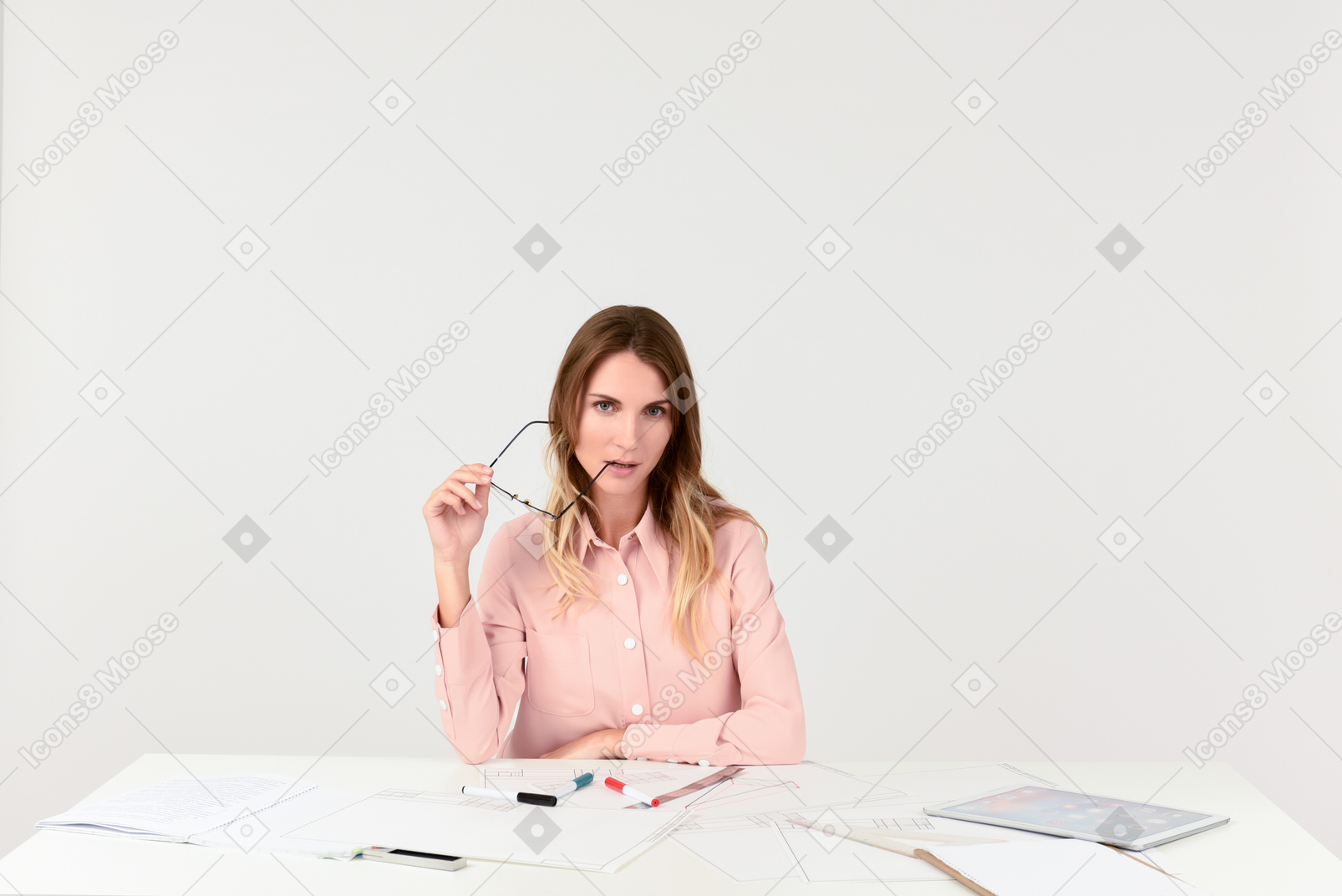 Female architect sitting at the table and bitting her eyeglasses