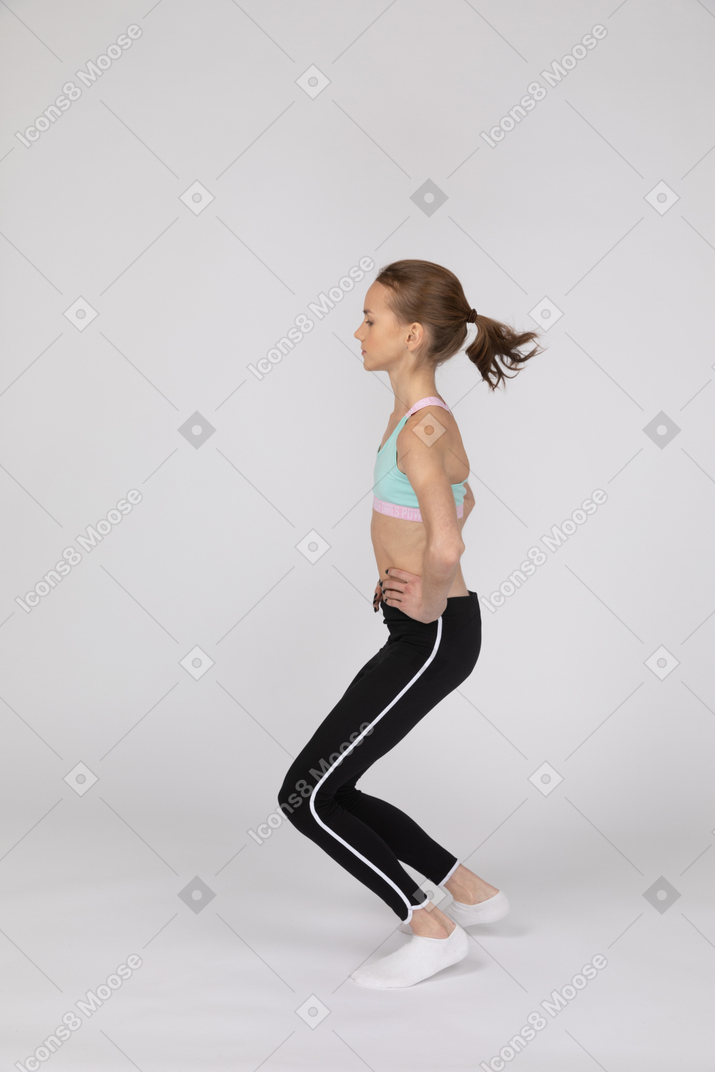 一个十几岁的女孩在运动服把双手哦臀部和弯曲的膝盖的侧视图