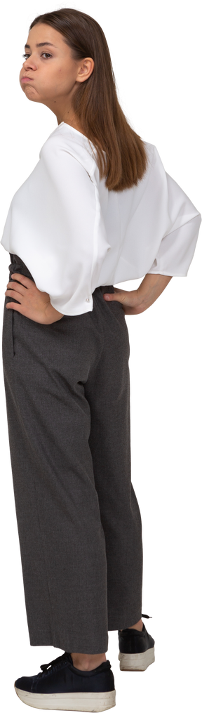 Vista posterior de tres cuartos de una joven en ropa de oficina soplando las mejillas y poniendo las manos en las caderas