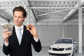 A man in a suit holding money next to a car