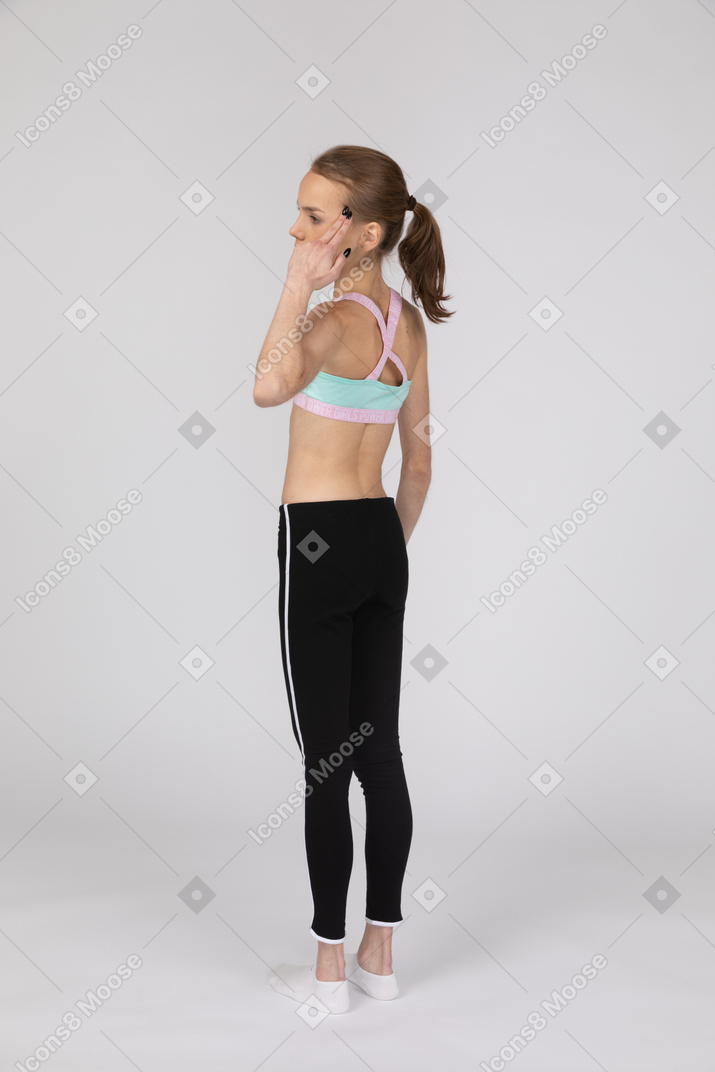 Vista traseira a três quartos de uma adolescente em roupas esportivas tocando a cabeça