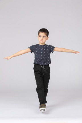 一个可爱的男孩在一条腿上保持平衡并伸出双臂的前视图