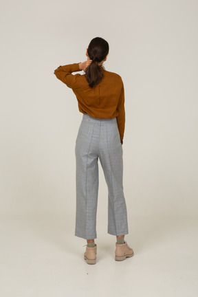 Back view of a young asian female in breeches and blouse touching neck