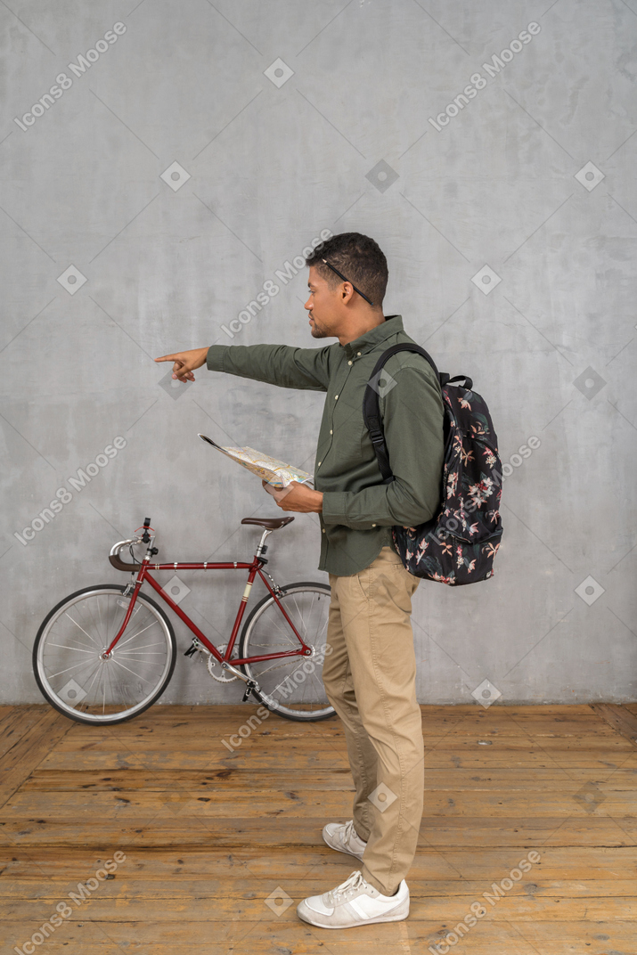Vista lateral de um homem com uma mochila olhando para um mapa e apontando para o lado