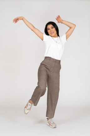 Front view of a dancing young lady in breeches and t-shirt raising hands