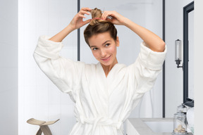 A woman standing in a bathroom putting her hair in a bun