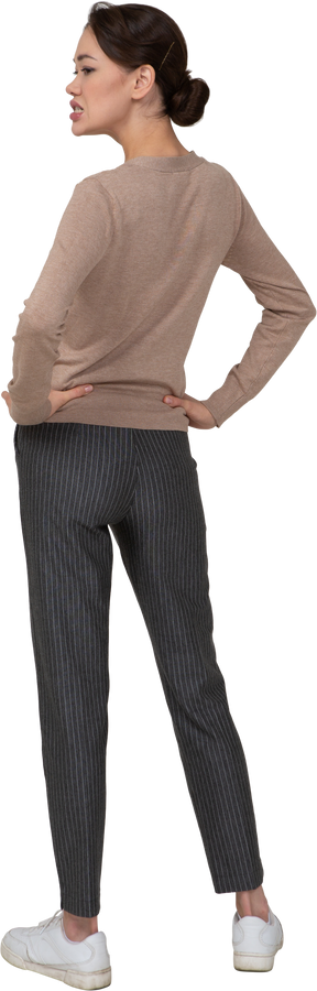 Vista posteriore di tre quarti di una giovane donna in pullover e pantaloni che mette le mani sui fianchi e stringe i denti