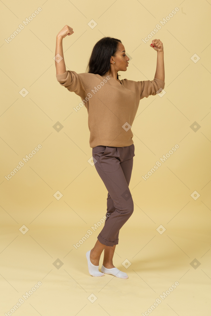 Three-quarter view of a dark-skinned young female raising hands and clenching fists