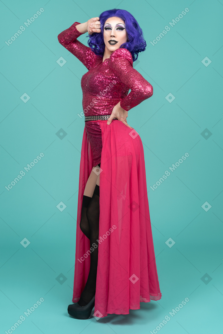 Drag queen posing with one hand on waist & the other raised up to face