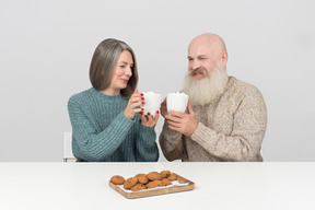 Gealtertes paar, das am tisch sitzt und beifall mit kaffeetassen sagt