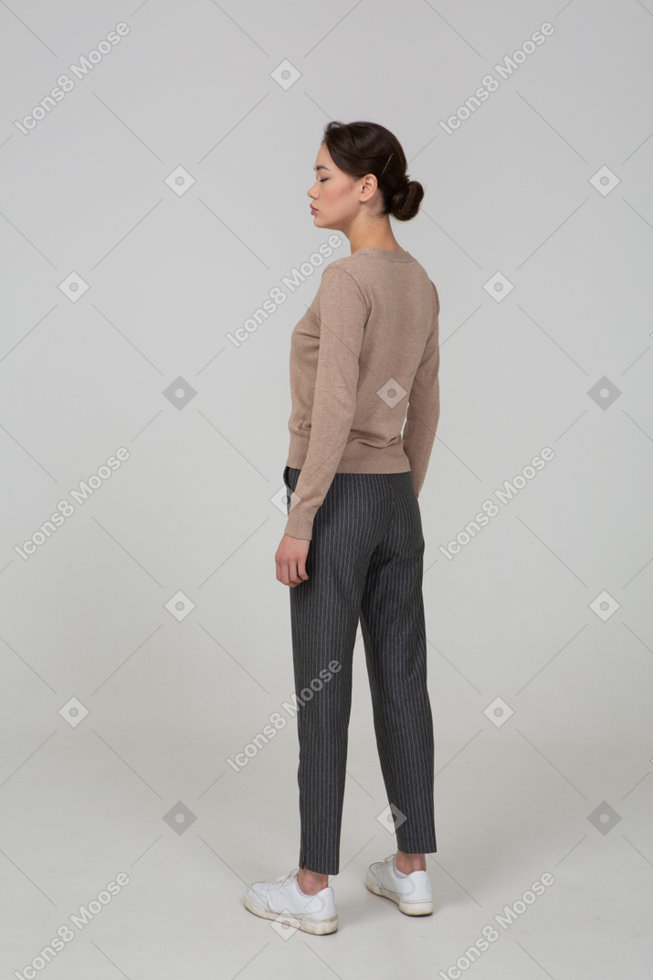 Vista de três quartos das costas de uma jovem parada em um pulôver e calças com os olhos fechados