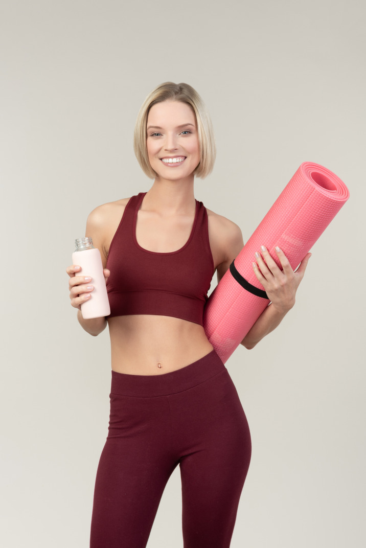 Young woman holding yoga mat and sport bottle