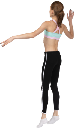Vista posterior de tres cuartos de una jovencita en ropa deportiva levantando la mano y saltando