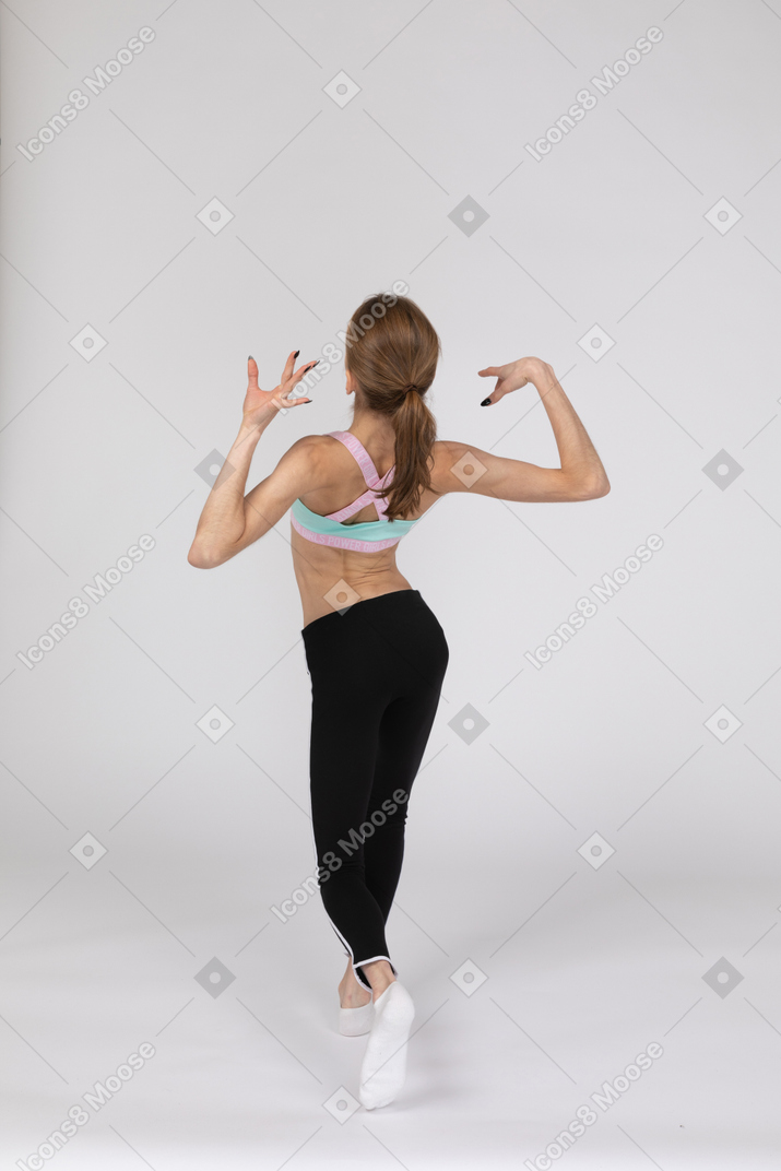 Vista posterior de tres cuartos de una elegante jovencita en ropa deportiva levantando las manos
