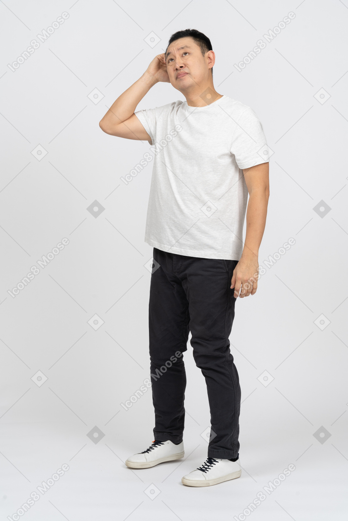 Vista frontal de un hombre con ropa informal rascándose la cabeza y mirando hacia arriba