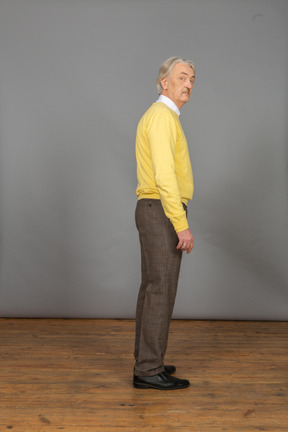 Vista lateral de un anciano curioso en jersey amarillo girando la cabeza y mirando a la cámara
