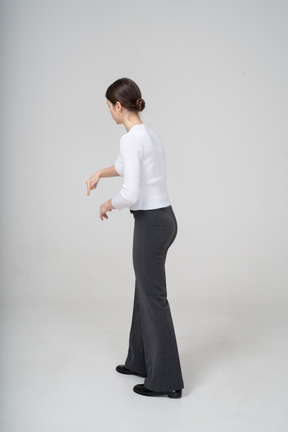 Side view of a young woman in black pants and white blouse pointing with a finger