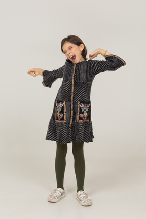 Vista frontal de una niña vestida estirando la espalda y los brazos