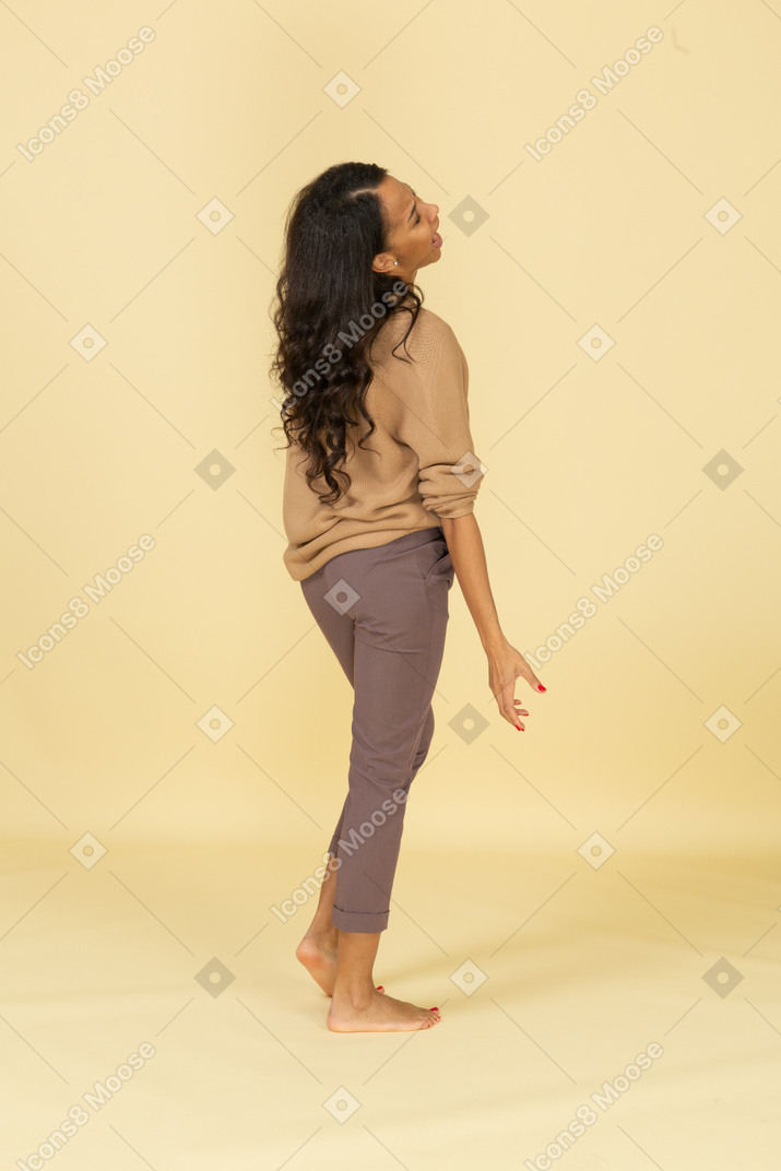 Three-quarter back view of a naughty dark-skinned young female outspreading hands