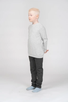 Un niño rubio con ropa casual de pie y escondiendo las manos detrás