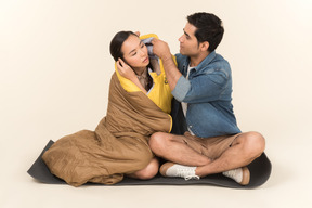 Young interracial couple sitting in sleeping bag and man adjusting girl's hair