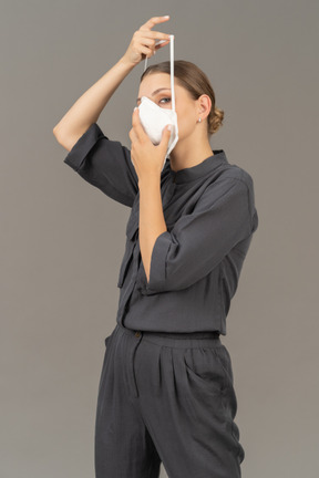 Woman in gray coveralls putting on a respirator