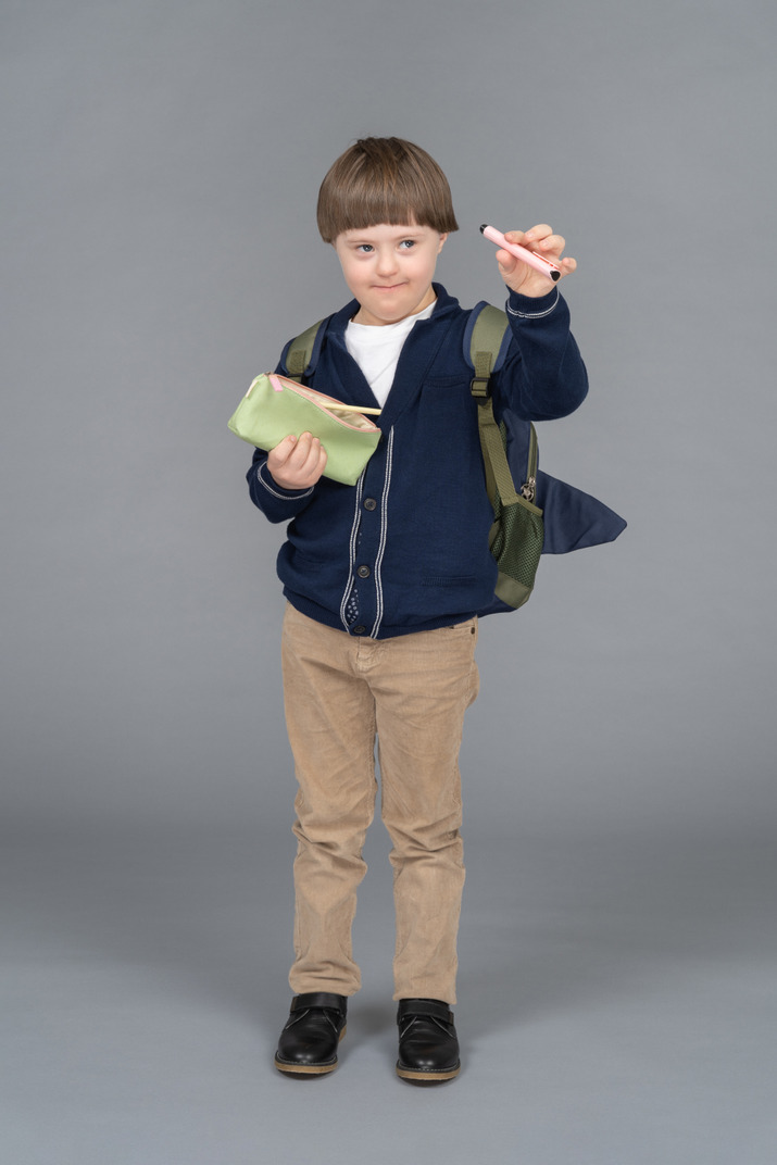 A little boy with a backpack holding a pencil case and a pen