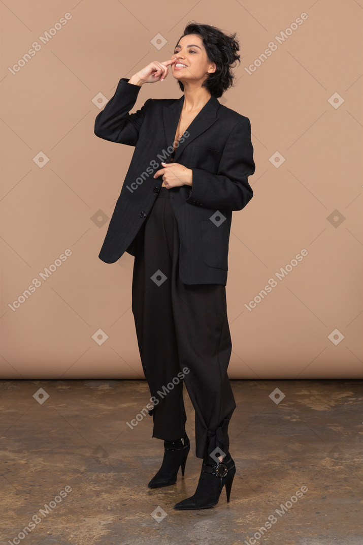 Three-quarter view of a funny businesswoman in a black suit touching her nose