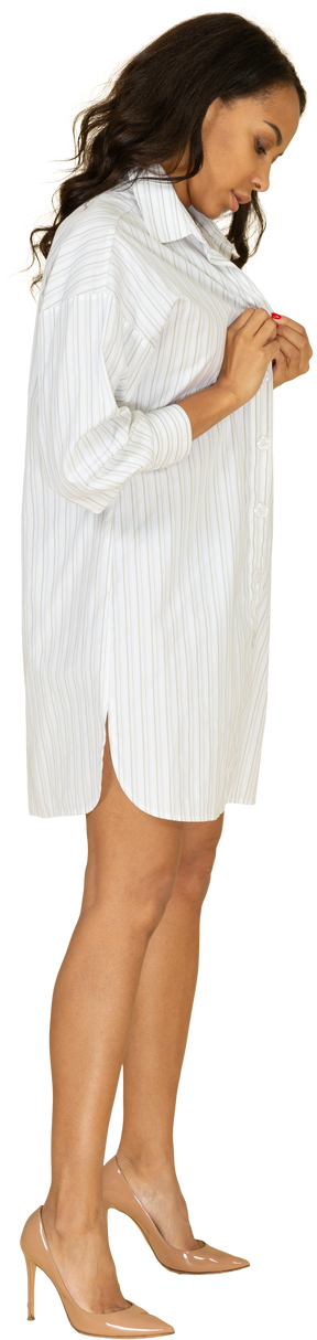 Vista lateral de una mujer joven de piel oscura abrochando su vestido blanco