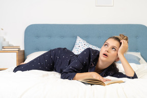 Vue de face d'un livre de lecture de jeune femme ennuyée au lit