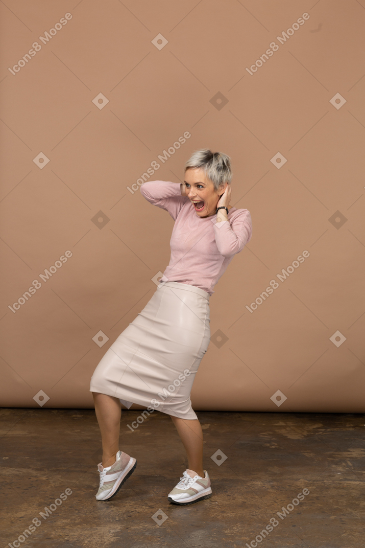 Vista frontal de una mujer feliz en ropa casual inclinándose hacia atrás con las manos detrás de la cabeza