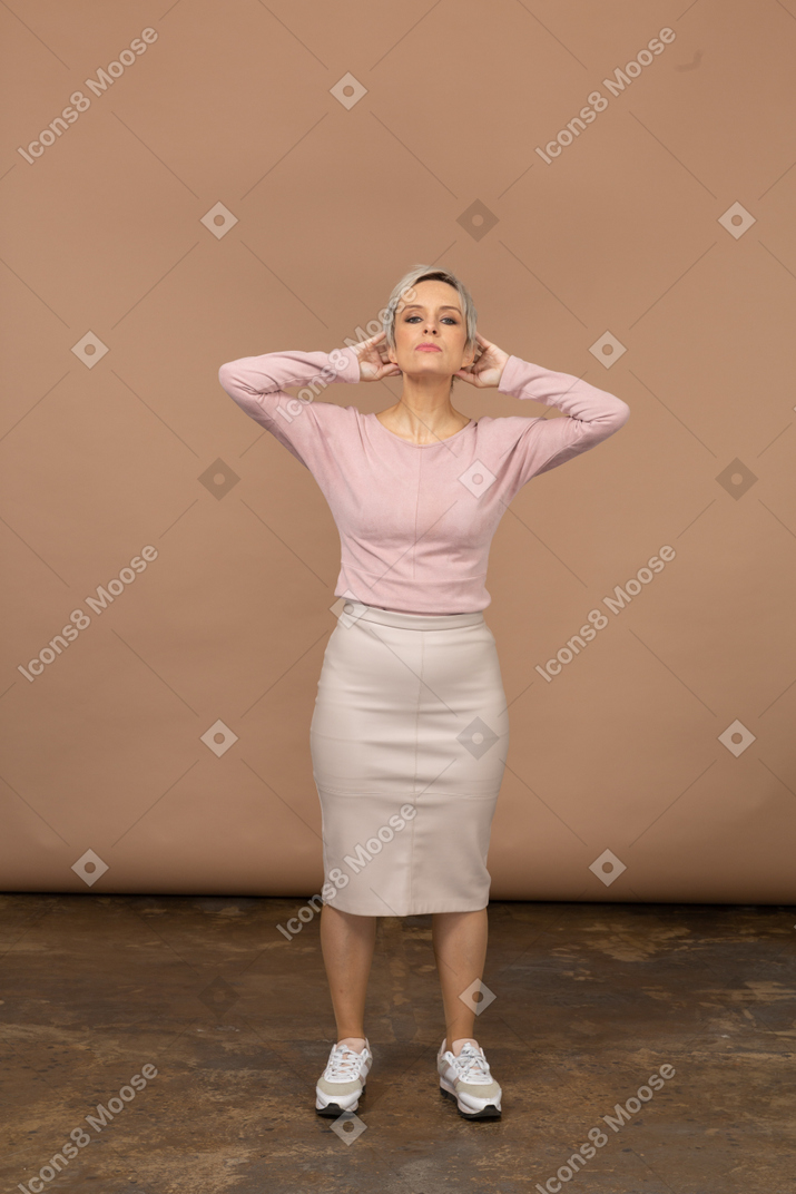 頭の後ろに手を置いて立っているカジュアルな服装の女性の正面図