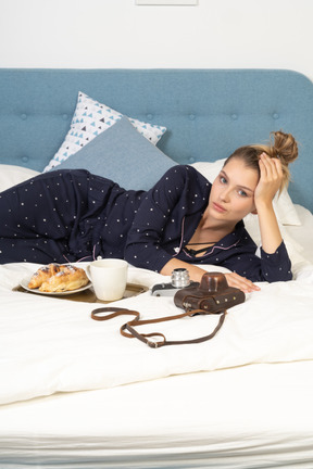 Vista frontal de uma jovem deitada na cama tomando café da manhã