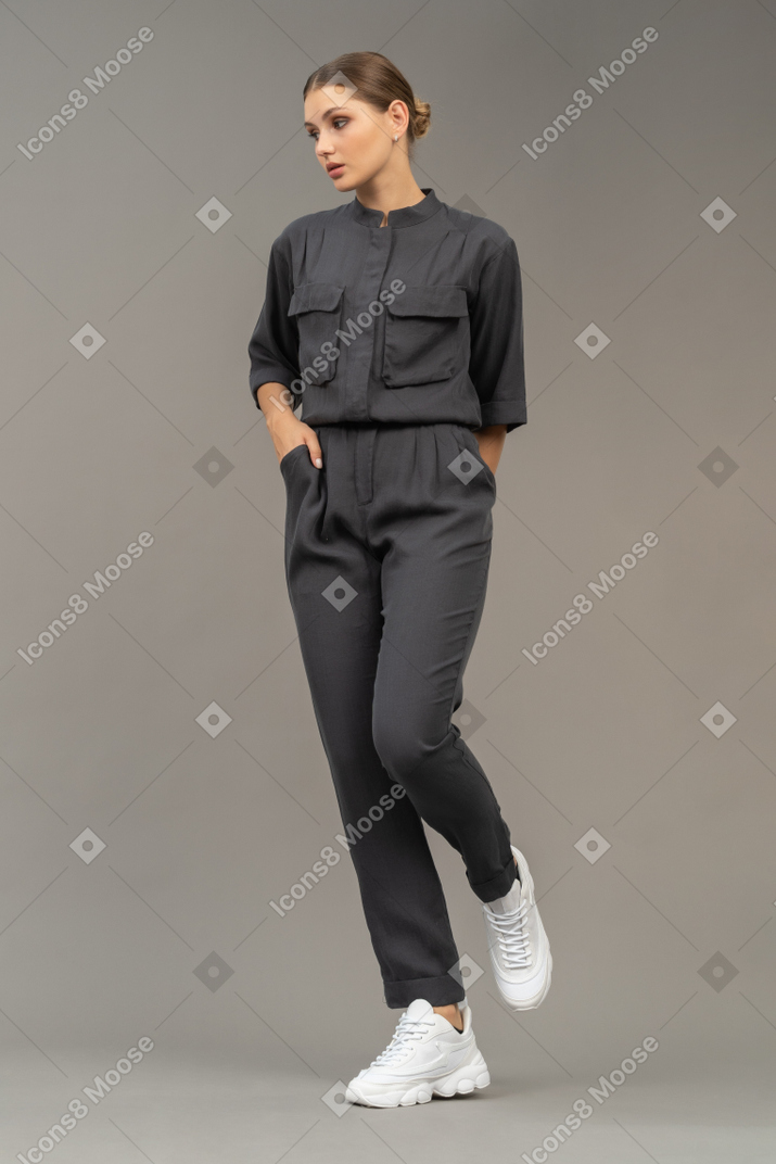 Front view of a walking young woman in a jumpsuit holding hand in pocket