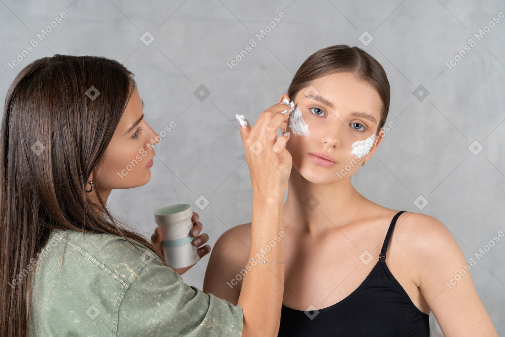 美容师在年轻女性脸上涂抹保湿霜