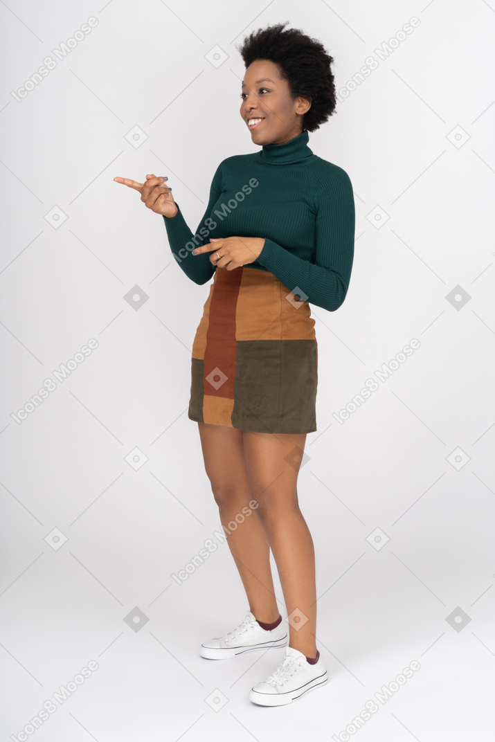 Sorridente garota afro-americana, apontando para o lado com o dedo