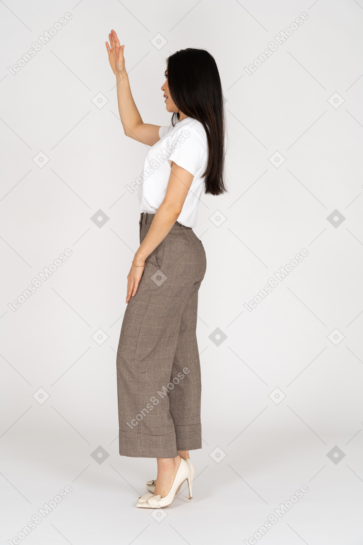 Vista laterale di una giovane donna saluto in calzoni alzando la mano