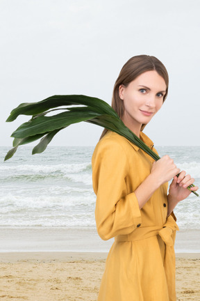 A woman standing on a beach holding a plant