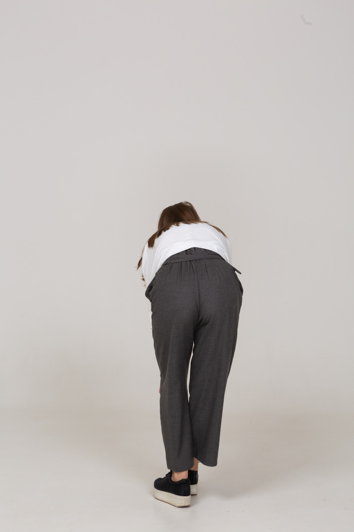 Back view of a young lady in office clothing bending down & touching knee