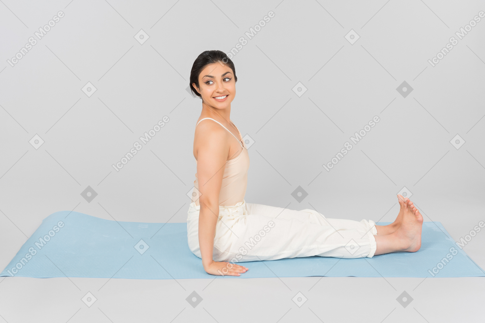 Junge indische frau, die mit der rückseite gerade auf yogamatte sitzt