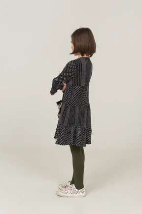 Three-quarter back view of an offended little girl in dress crossing arms
